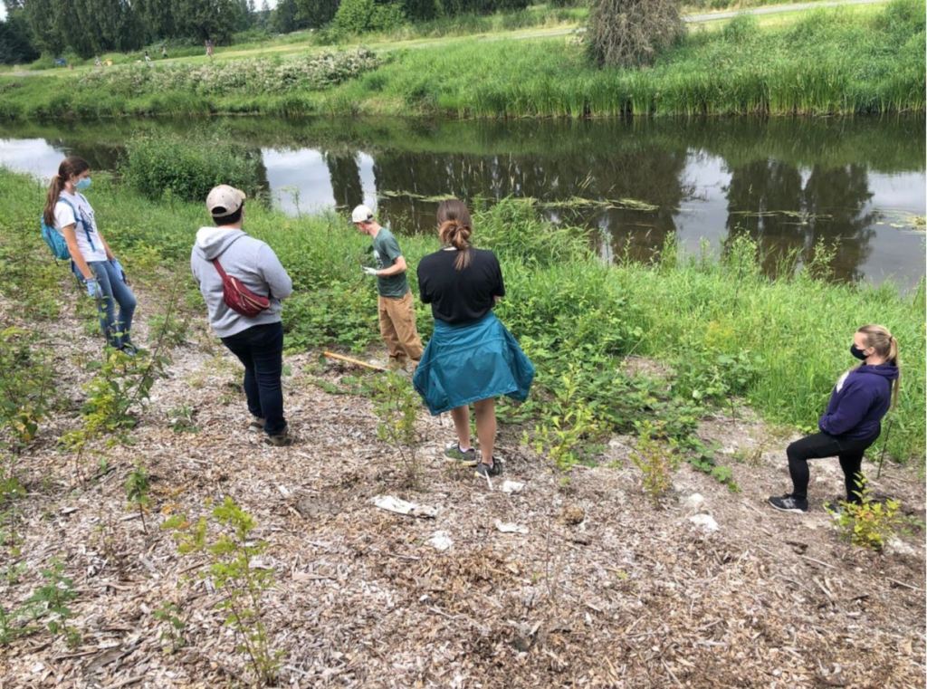 People standing in an area along a river bank with plants and mulch